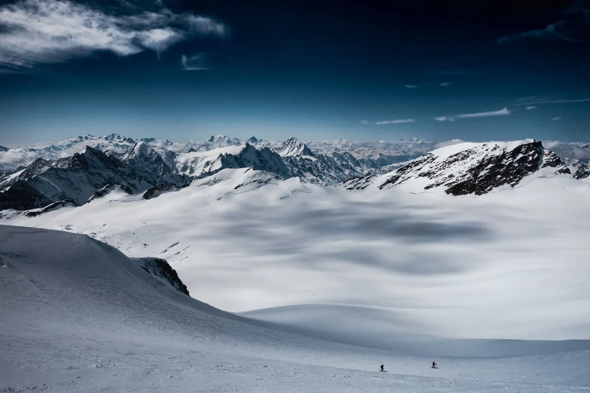 Zwei Skitourengeher auf einem weiten Gletscher vor einem Alpenpanorama